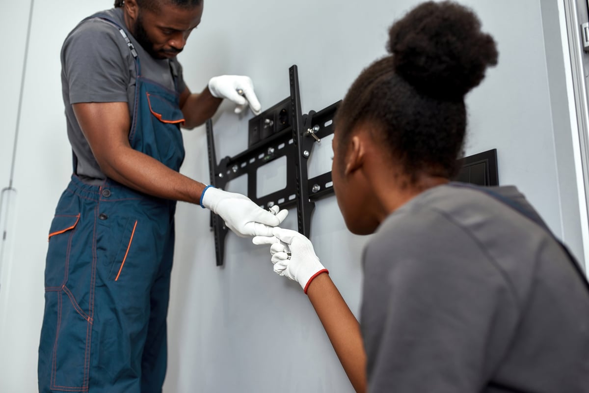 Two people mounting a TV on a living room wall